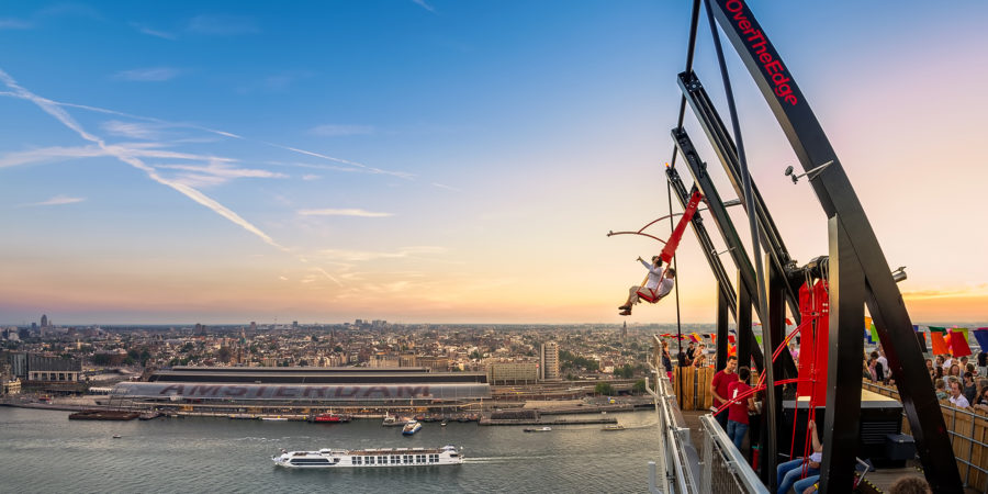 Over The Edge at Lookout Amsterdam at sunset: a rider swung out over the edge of the tower, with the IJ and the city behind
