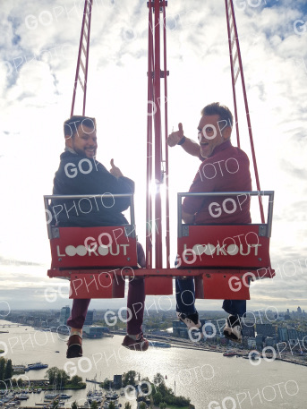 Two men composited onto the ledge at sunset, thumbs up with the A'DAM tower behind them