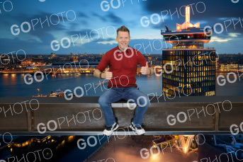 A man composited onto the Lookout ledge at dusk, the lit-up A'DAM tower behind him